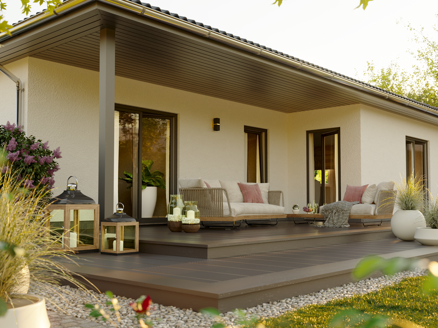 Winkelbungalow 108 – Detailansicht Terrasse mit Verschattung im Tageslicht Frontale Nahaufnahme der Terrasse des Winkelbungalow 108 mit bodentiefen Fenstern, modernen Sitzmöbeln und Blumenschmuck bei Tageslicht.